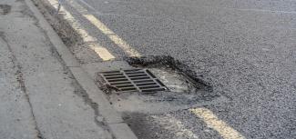 Road breaking up around gully grate installation creating a pothole
